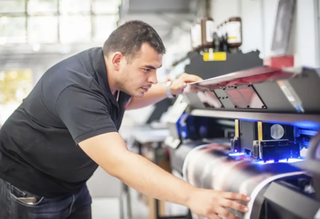 Homem operando uma impressora industrial, explorando o custo do outsourcing de impressão em ambiente profissional. A imagem destaca o uso da tecnologia na impressão.